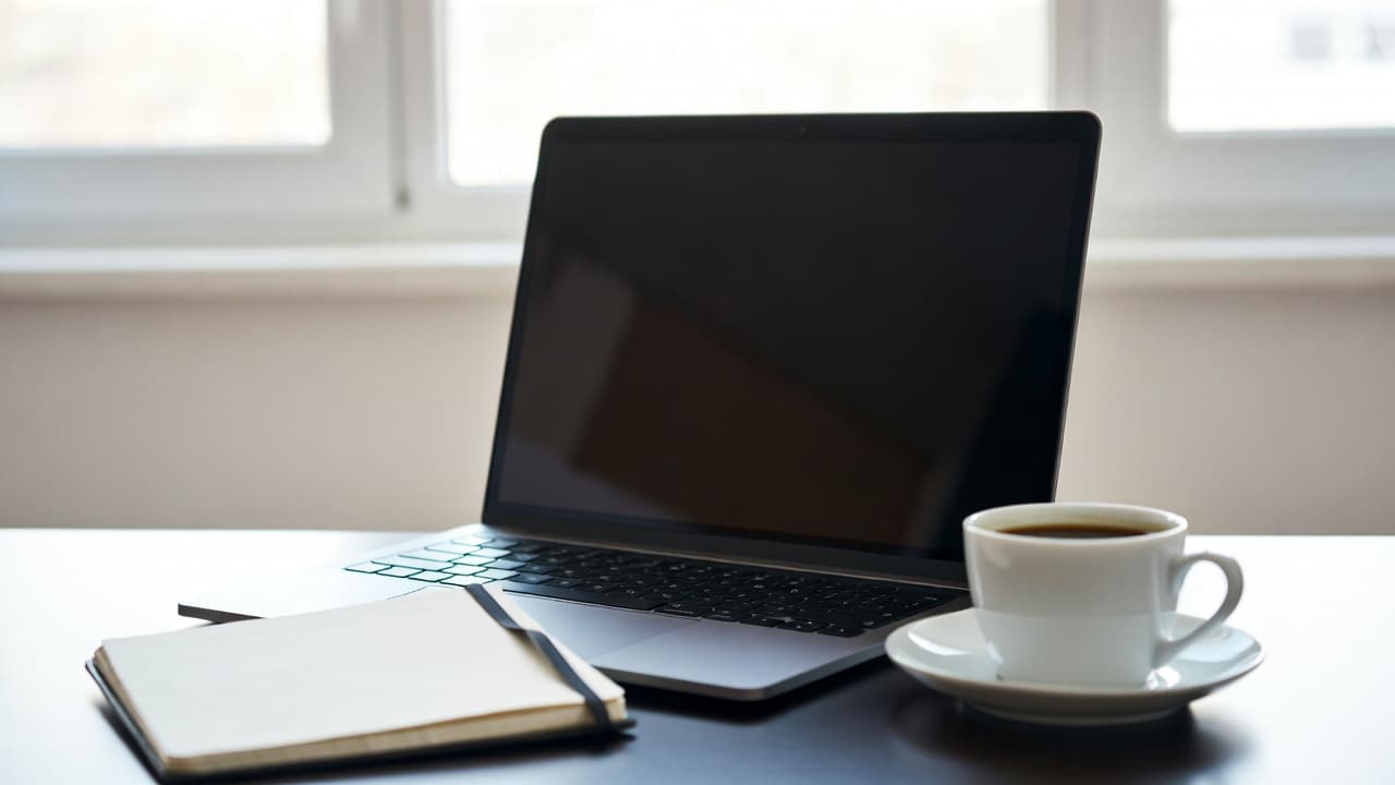 Minimalistischer Arbeitsplatz mit Laptop und Notizbuch für einfache Zeiterfassung